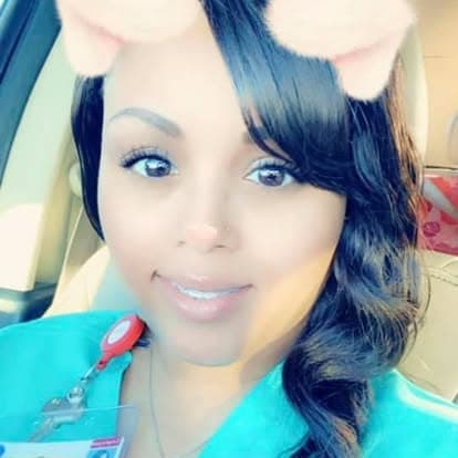 Smiling woman wearing teal medical scrubs and a cat ear filter while in a car.